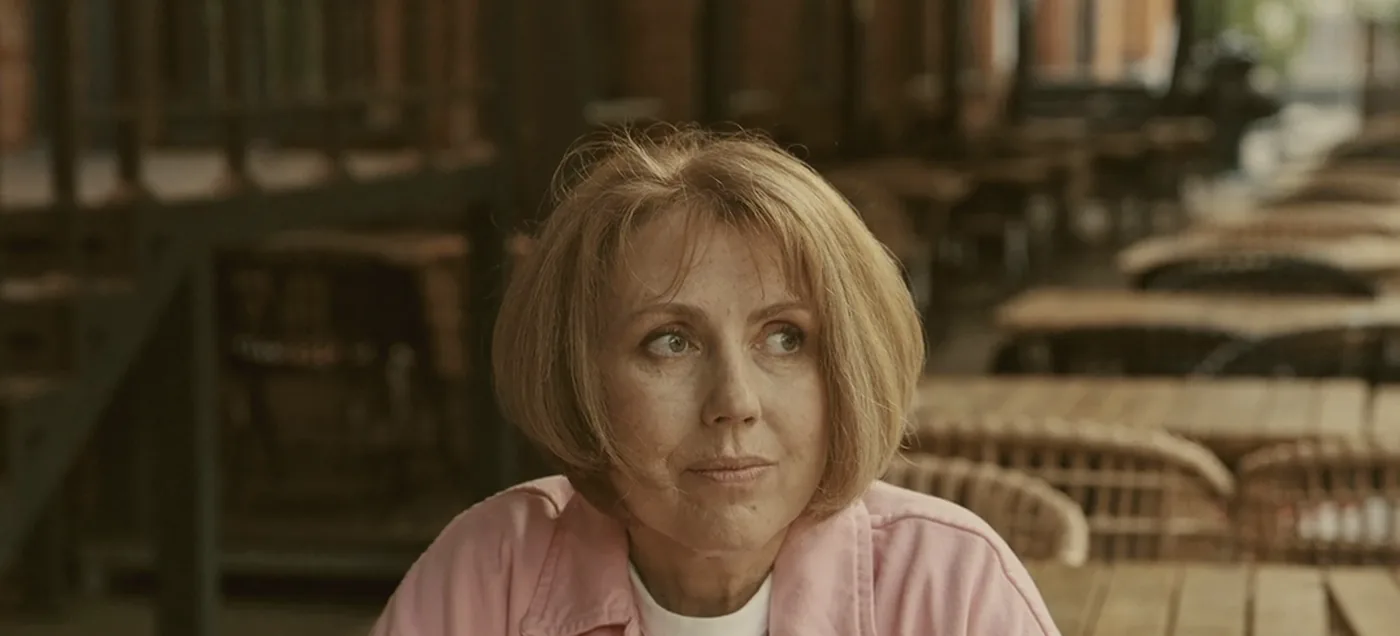 A woman sitting alone with her phone at a long row of empty café tables.
