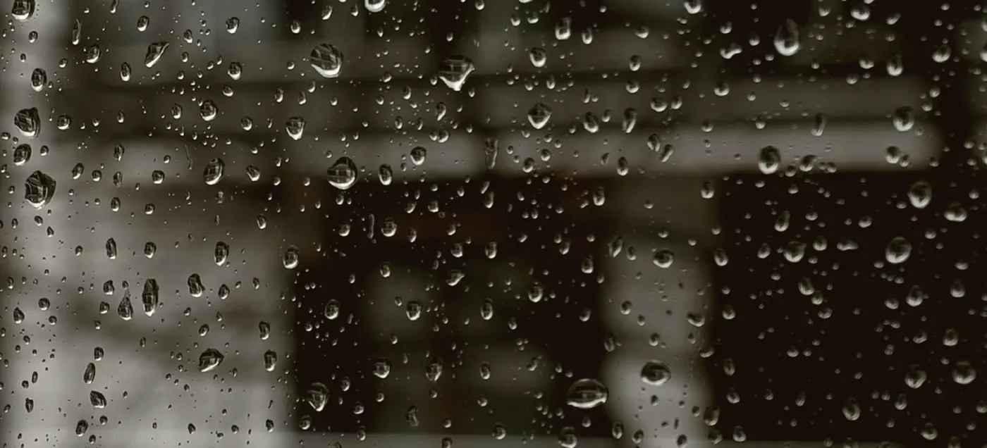 Rain beading on a window with lights blurred behind it.