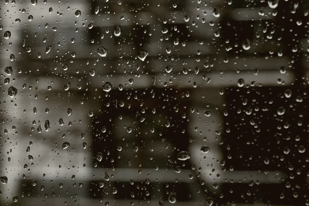 Rain beading on a window with lights blurred behind it.