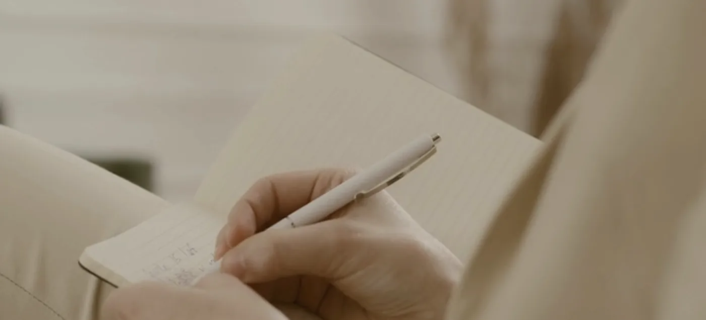 Hands writing a short note in a notebook.