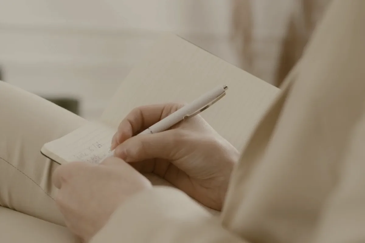 Hands writing a short note in a notebook.